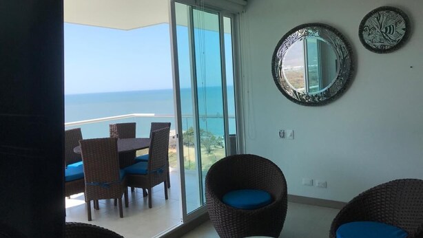 A balcony with a view of the sea, wicker chairs with blue cushions, and two wall mirrors. - Apartamento Amoblado Playa Dormida Santa Marta (Santa Marta)
