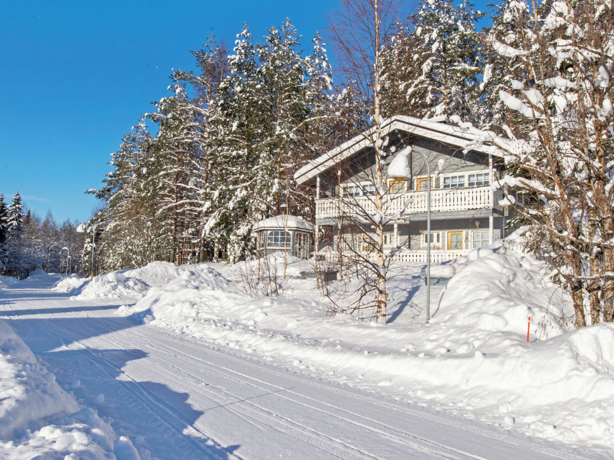 Ein schneebedecktes Gebäude mit Balkon, umgeben von Bäumen und einer verschneiten Straße.
