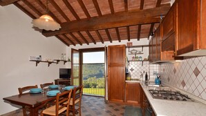 Une cuisine avec des meubles en bois, une table à manger avec des chaises, une vue à travers une porte vitrée et un pare-feu en carreaux.