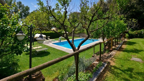 Une piscine entourée d’une clôture en bois, avec une pelouse verdoyante et des arbres en arrière-plan.