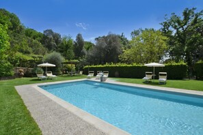 Une piscine rectangulaire bordée d’une terrasse, entourée d’une pelouse bien entretenue et d’arbres.