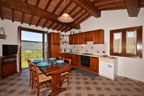 A kitchen with wooden cabinets, a dining table with chairs, a TV, and a view through a large window.