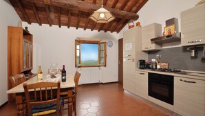 Une cuisine avec des meubles en bois, une table à manger avec des chaises, un luminaire suspendu et une vue par la fenêtre.