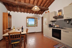 Une cuisine avec des meubles en bois, une table à manger avec des chaises, un luminaire suspendu et une fenêtre donnant sur un beau paysage.