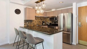 A modern kitchen with a central island, bar stools, stainless steel appliances, and a clock on the wall. - Woodrun Lodge w/ pool & gym (Whistler)