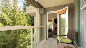 A balcony with a view of trees, a wicker chair, and a door leading to an interior space. - Woodrun Lodge w/ pool & gym (Whistler)