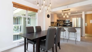 A modern kitchen with a dining area, large windows, and a view of the outdoors. - Woodrun Lodge w/ pool & gym (Whistler)