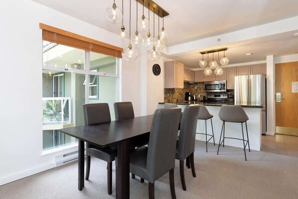 A modern kitchen with a dining area, large windows, and a view of the outdoors.