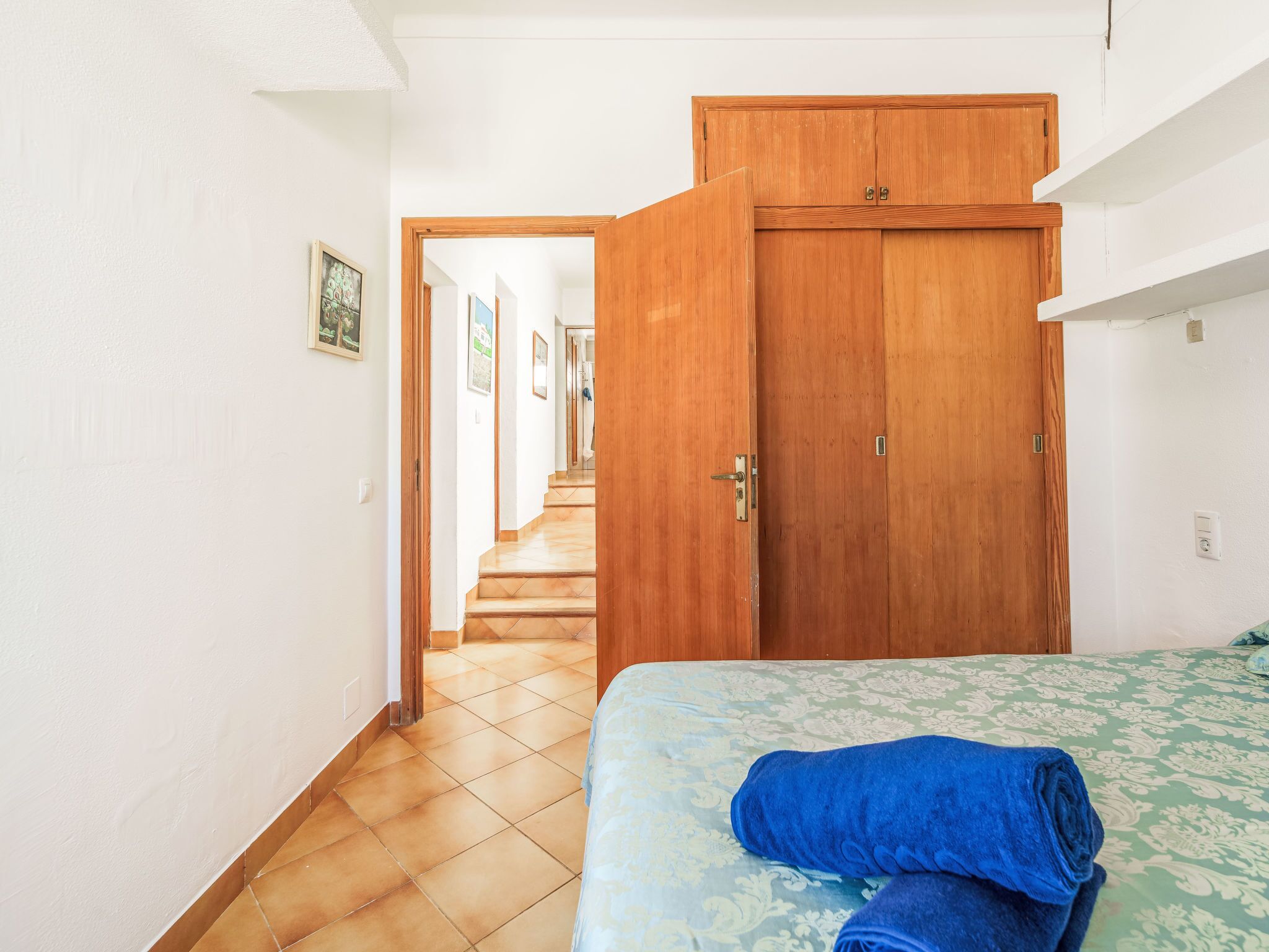 Una habitación de hotel con una cama, un armario de madera y un pasillo que lleva a otra habitación.