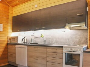 A modern kitchen with wooden paneling, a built-in microwave, a coffee machine, a sink, and a stove.