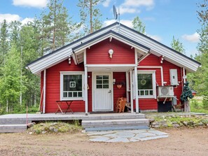 A red cabin with a white door, windows, and a porch with chairs.