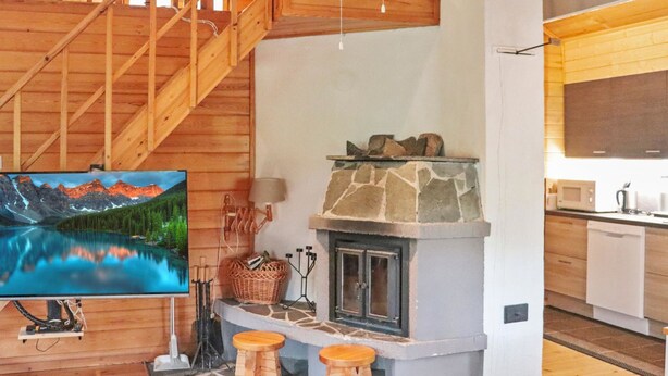 A wooden interior with a stone fireplace, a wooden staircase, and a kitchen area.
