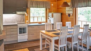 A compact kitchen with a stove, oven, and refrigerator, wooden walls, and a dining area with a table and chairs.