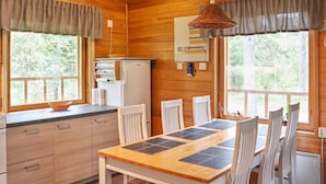 A wooden cabin interior with a kitchen, dining area, and large windows.