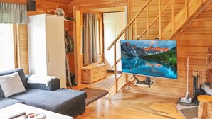 A wooden cabin interior with a living area, a staircase, and a TV displaying a mountain landscape.