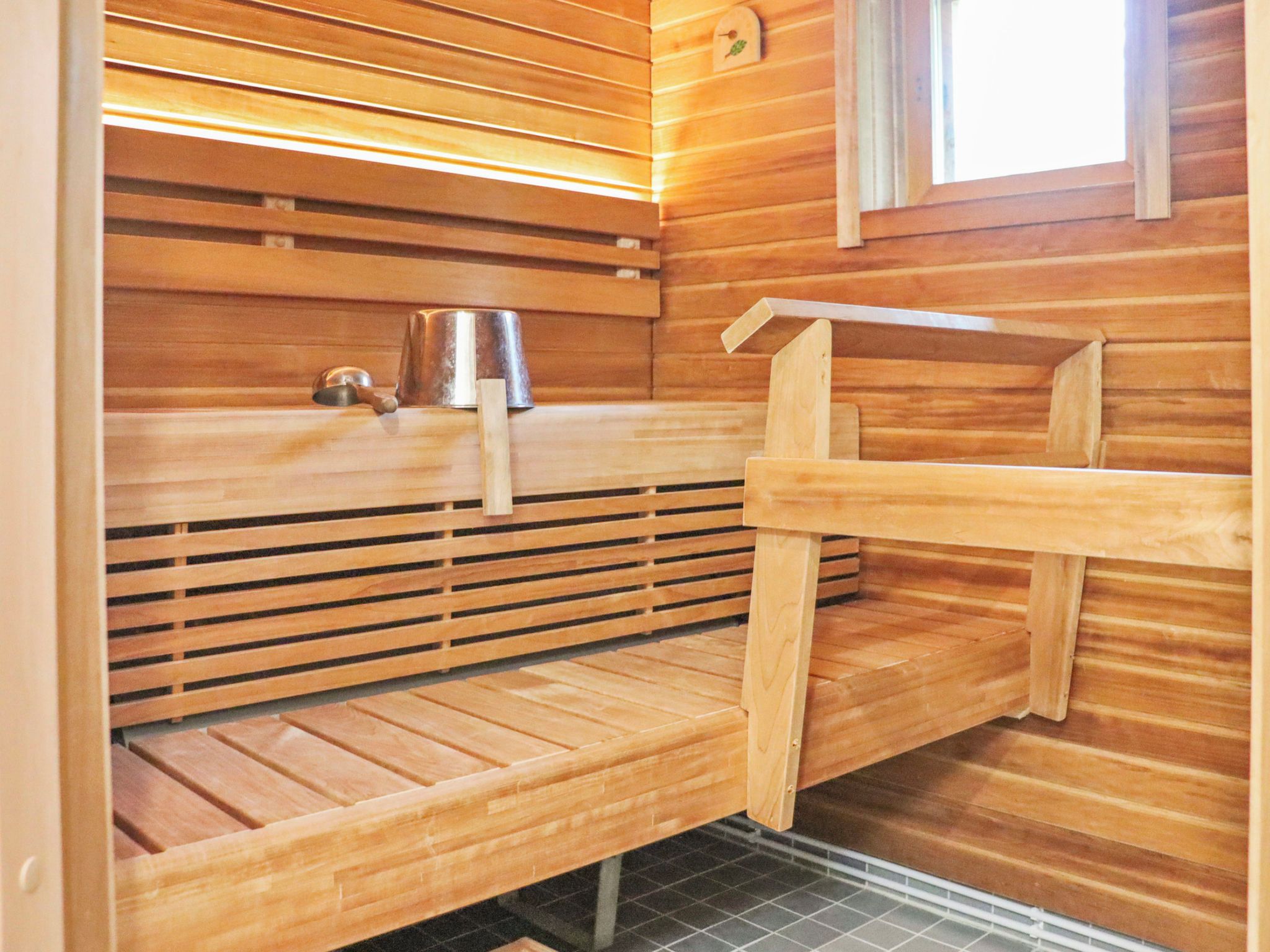 A sauna room with wooden benches, a metal bucket, and a towel rack.
