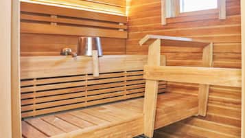A sauna room with wooden benches, a metal bucket, and a towel rack.
