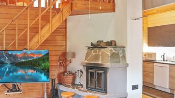 Un interior de madera con chimenea de piedra, escalera de madera y zona de cocina.
