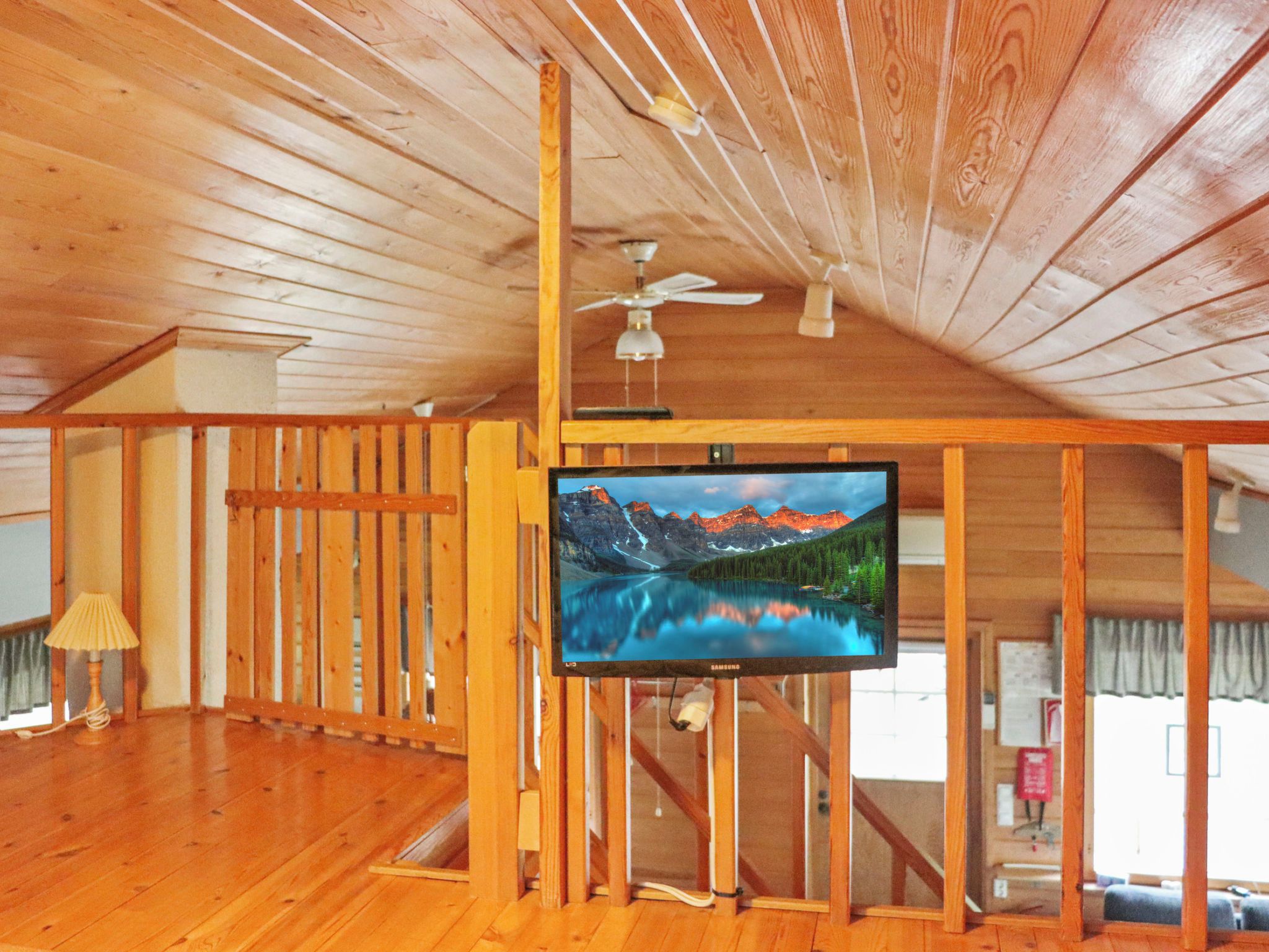 A room with wooden walls and ceiling, a ceiling fan, a mounted TV, and a wooden floor.