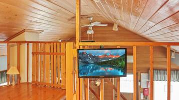 A room with wooden walls and ceiling, a ceiling fan, a mounted TV, and a wooden floor.
