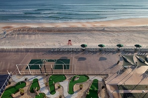Eine Luftaufnahme eines Strandes mit Sportplatz, Liegestühlen und Sonnenschirmen.