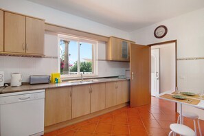 Une cuisine avec des meubles de rangement en bois, un lave-vaisselle, une fenêtre et un coin repas comprenant une table et des chaises.