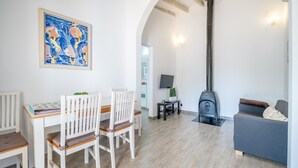 A living room with a white table, chairs, a sofa, a painting, a TV, and a wood-burning stove. - Vacation Home Ses Oliveres with Mountain View, Wi-Fi, A/C, Terraces & Garden (Pollença)