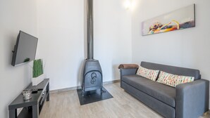 A living room with a sofa, a flat-screen TV, a fireplace, and a painting on the wall. - Vacation Home Ses Oliveres with Mountain View, Wi-Fi, A/C, Terraces & Garden (Pollença)