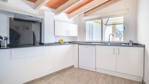 A modern kitchen with white cabinets, a dishwasher, and a window with blinds. - Vacation Home Ses Oliveres with Mountain View, Wi-Fi, A/C, Terraces & Garden (Pollença)