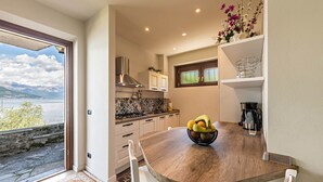 A modern kitchen with a wooden table, white cabinets, and a view of the outdoors. - Holiday Apartment "La Punta Bellagio" with Lake View, Wi-Fi, Garden & Terrace (Bellagio)