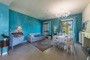 Une pièce aux murs de couleur turquoise, avec un canapé blanc, une table à manger et des chaises, un lustre et une fenêtre avec des rideaux.
