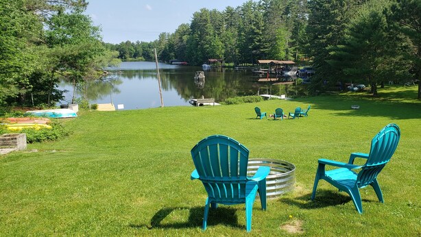 A grassy area with two blue Adirondack chairs and a metal fire pit.