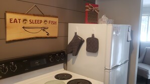 A kitchen with a stove, oven, and a refrigerator. There is a sign on the wall that reads "EAT SLEEP FISH".