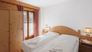 A bedroom with two beds, wooden wardrobe, bedside lamps, and a window with curtains. - Holiday Apartment "Ciasa Lino Rotic" with Mountain View and Wi-Fi (San Giovanni di Fassa)