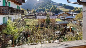 A traditional chalet with a balcony, a village below, and mountains in the background. - Holiday Apartment "Ciasa Lino Rotic" with Mountain View and Wi-Fi (San Giovanni di Fassa)