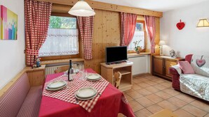 A cozy room with a dining table set for two, a television, and a sofa. - Holiday Apartment "Ciasa Lino Rotic" with Mountain View and Wi-Fi (San Giovanni di Fassa)