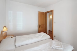 Un dormitorio con dos camas, una mesita de noche con lámpara y una puerta de madera que da a otra habitación.