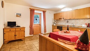 Una cocina compacta con armarios de madera, un comedor con mantel rojo y un televisor pequeño sobre un mueble de madera.