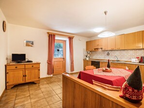 Une cuisine compacte avec des meubles en bois, un coin repas avec une nappe rouge et un petit téléviseur posé sur un meuble en bois.