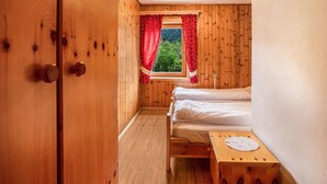 Una habitación de madera con una cama, una ventana con cortinas rojas y una pequeña mesa de madera con un mantel de encaje.