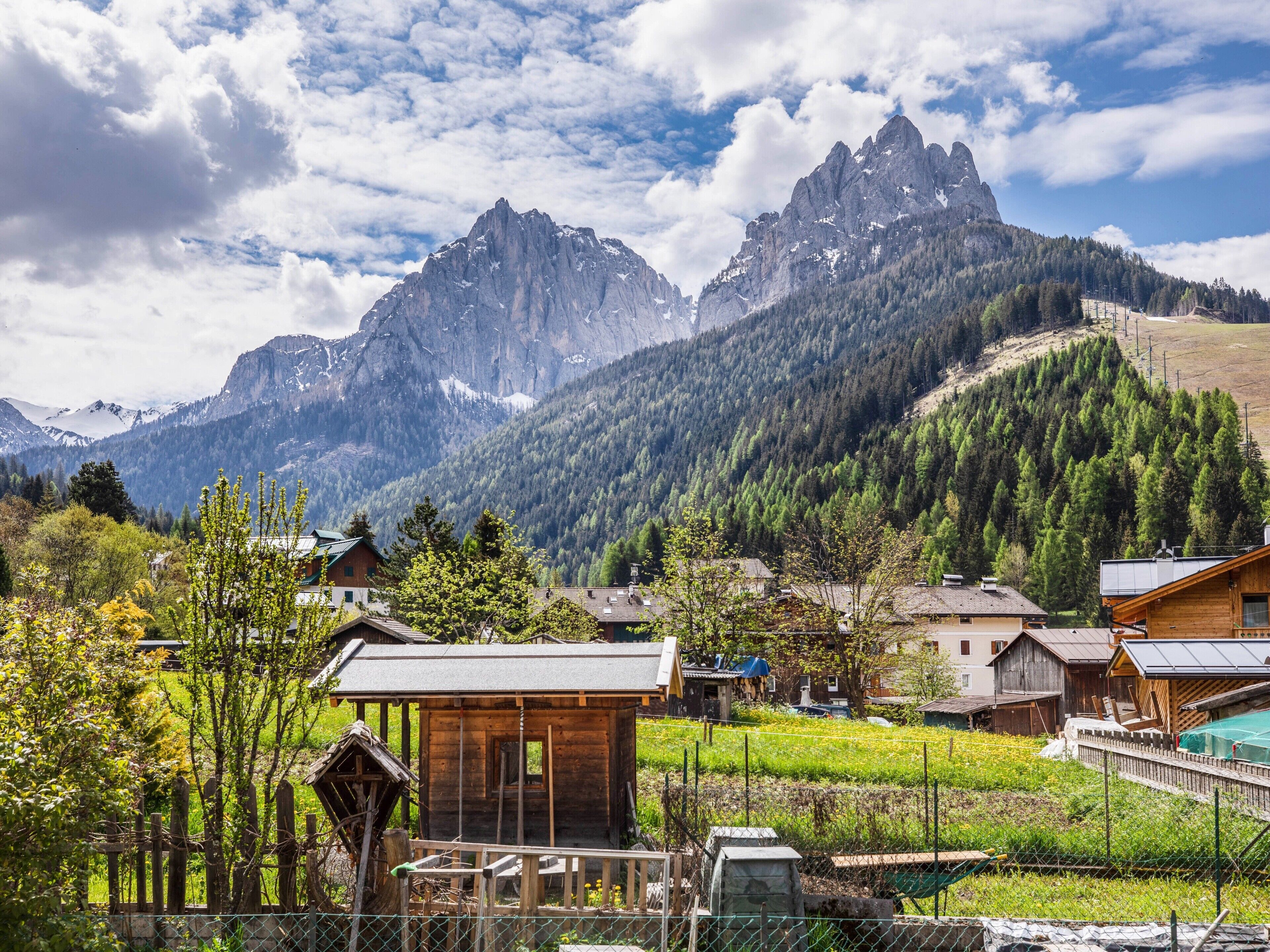 Un borgo montano con case in legno tradizionali, una baita di legno e vista sulle montagne rocciose.