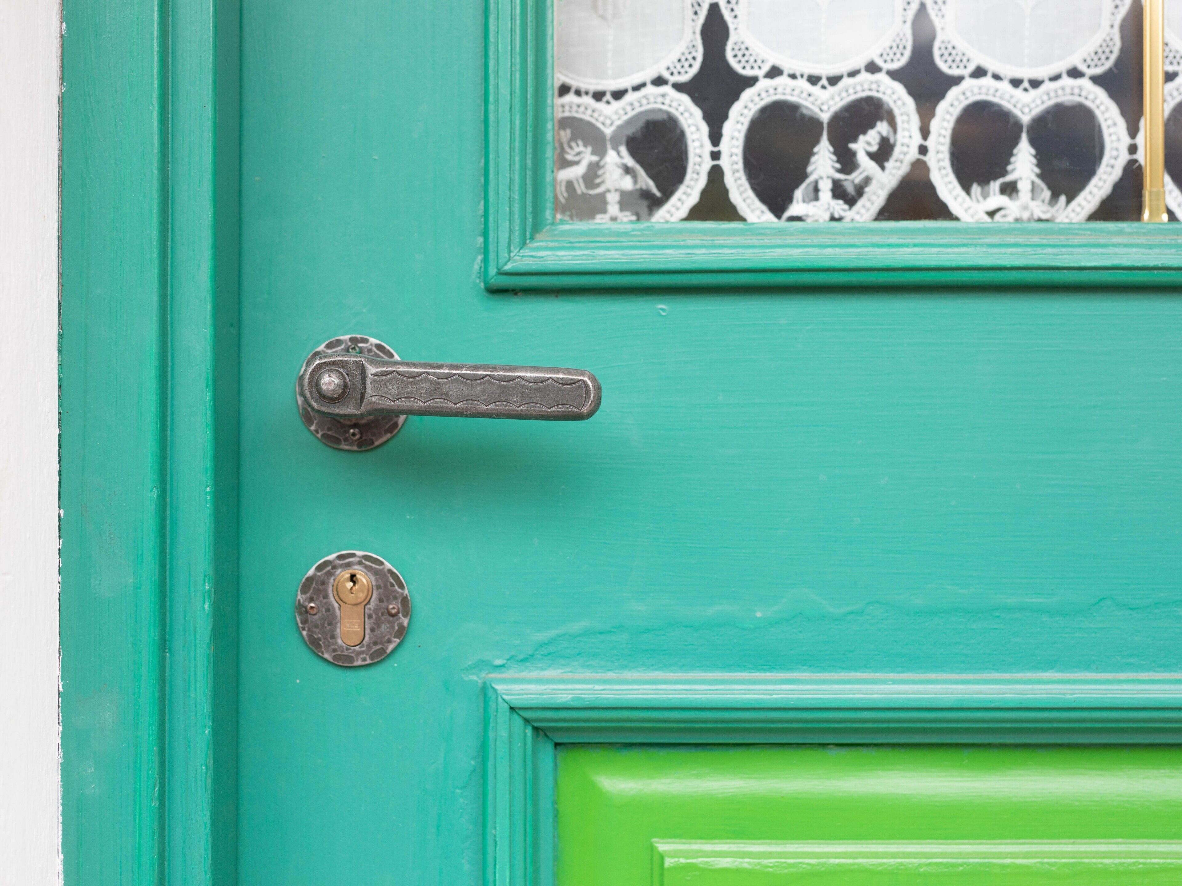 A teal door with a brass handle and a keyhole, and a decorative glass panel with heart motifs.