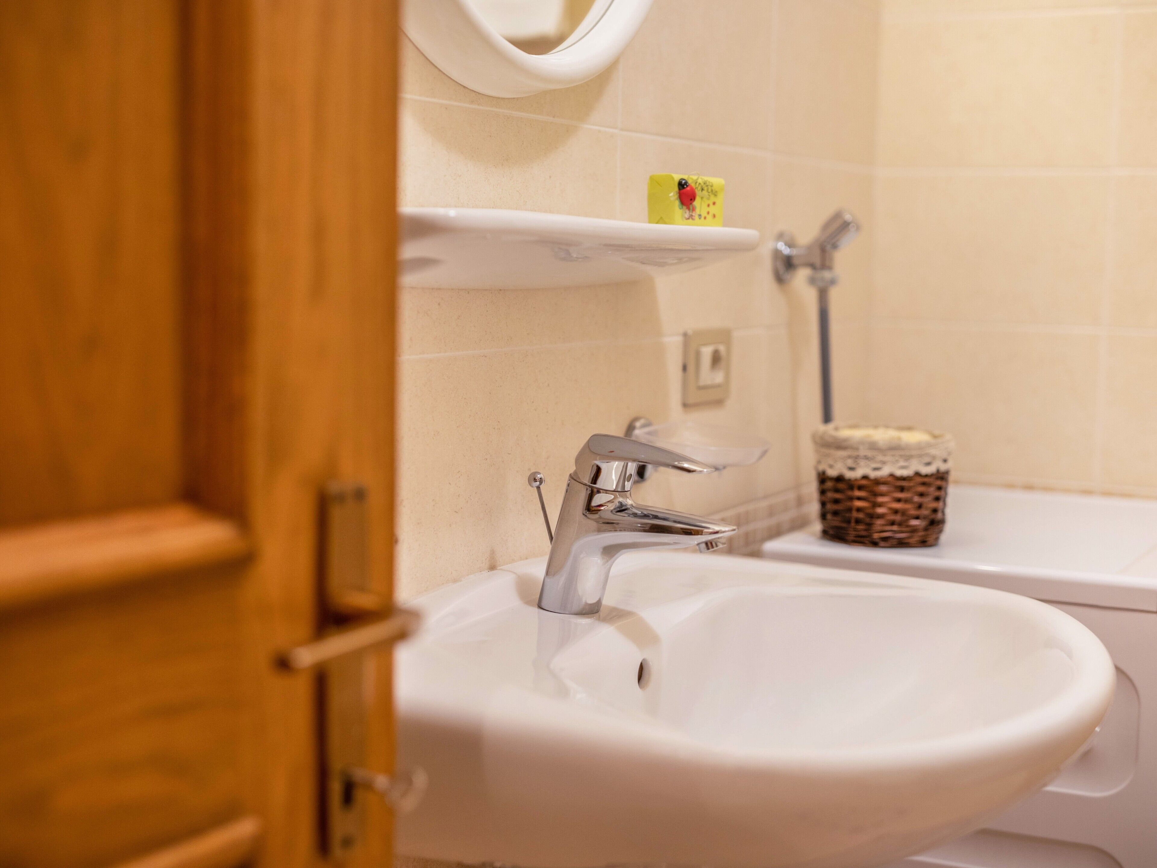 Une salle de bain avec un lavabo blanc, un miroir au-dessus et une étagère sur laquelle se trouve un distributeur de savon.