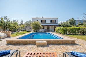 A swimming pool with stone tiles, a lounge area with chairs, and a two-story house with a tiled roof. - Country House 'La Palmera' with Mountain View, Wi-Fi and Air Conditioning (Pollença)