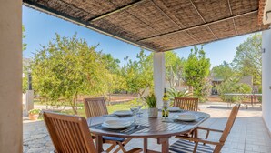 A covered outdoor dining area with a round table, chairs, and a bottle of wine.