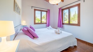 A bedroom with a bed, two windows with curtains, a hanging light fixture, and a nightstand with a lamp.