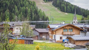 Un pueblo rural con casas de madera tradicionales, una iglesia y un telesilla al fondo.