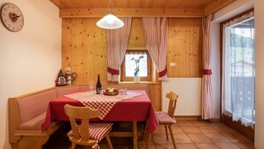 Un comedor acogedor con interior de madera, una mesa cubierta con mantel rojo, sillas y una botella de vino.