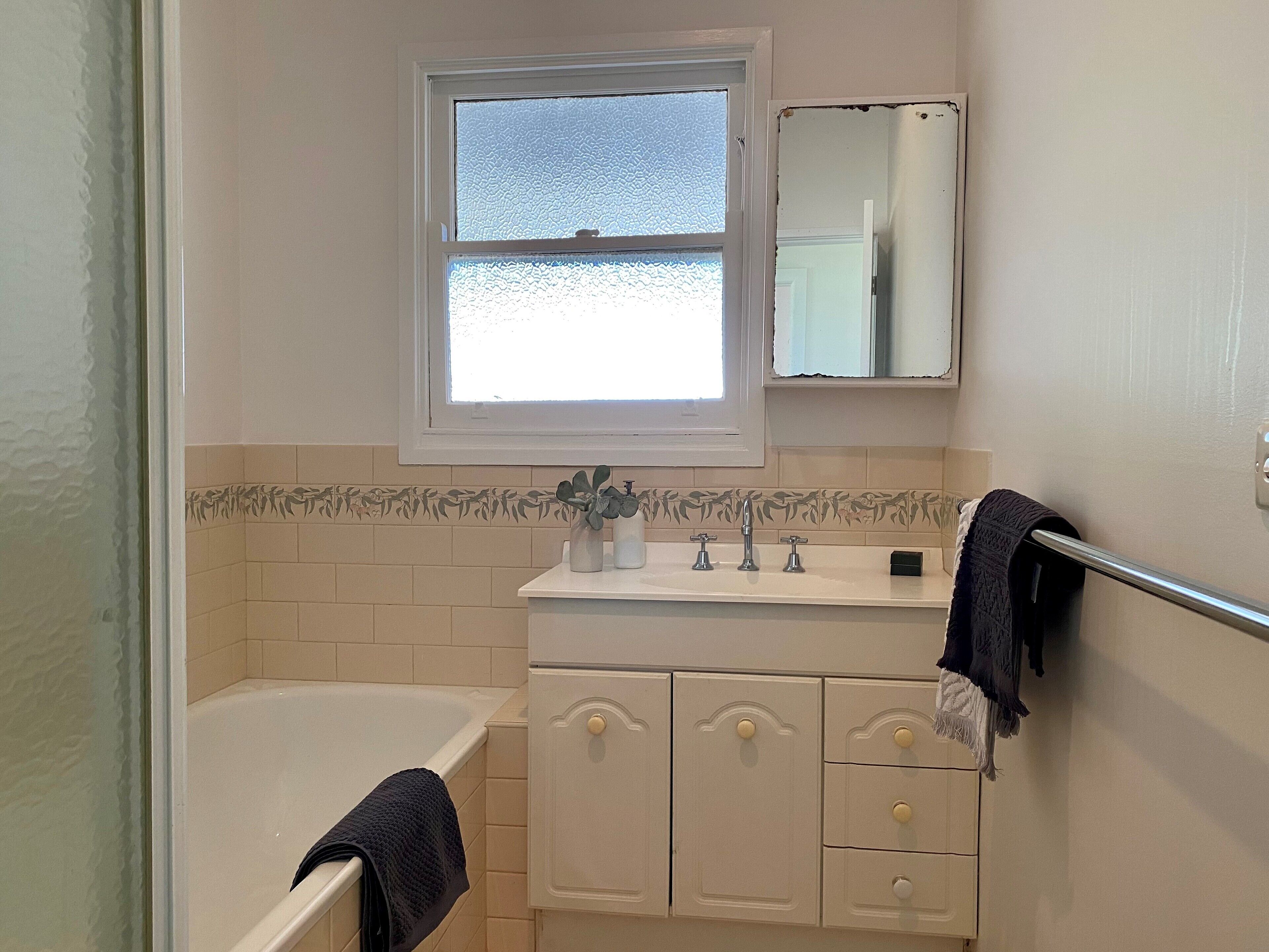 A bathroom with a bathtub, a sink with a mirror above it, and a towel rack.