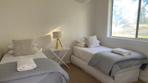 Hotellihuone, jossa on kaksi sänkyä, pieni pöytä lampun kanssa ja suuri ikkuna.